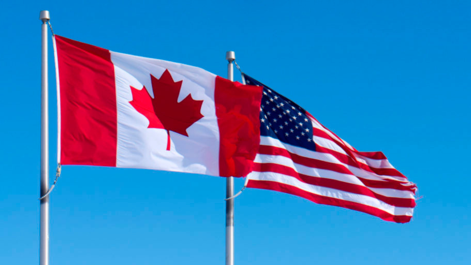 Canadian and American flags positioned side by side against a cloudy sky, symbolizing the cross-border trade relationship affected by the new tariffs