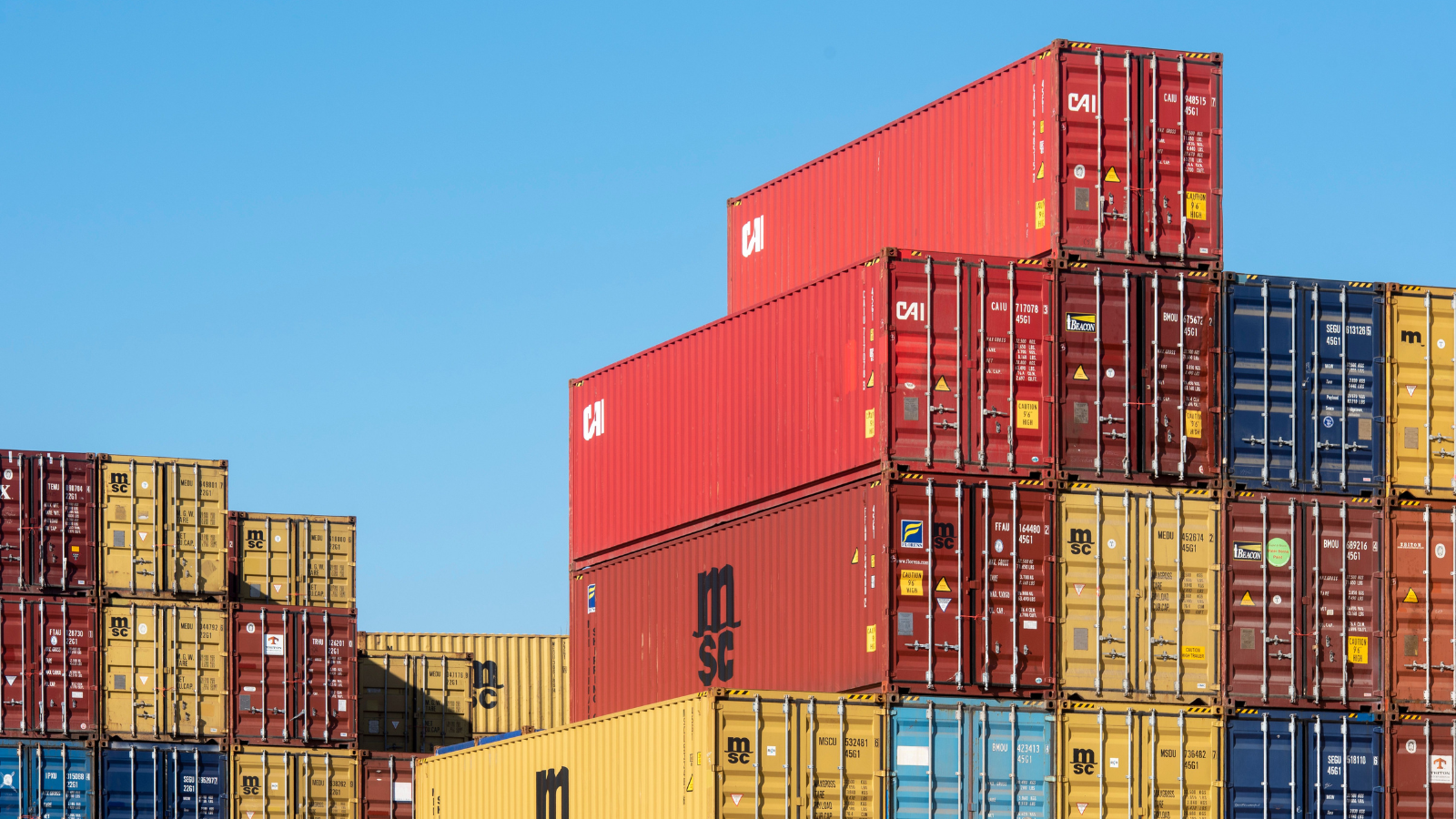 Stacked shipping containers at a port, representing cross-border import goods affected by the new food supply tariffs