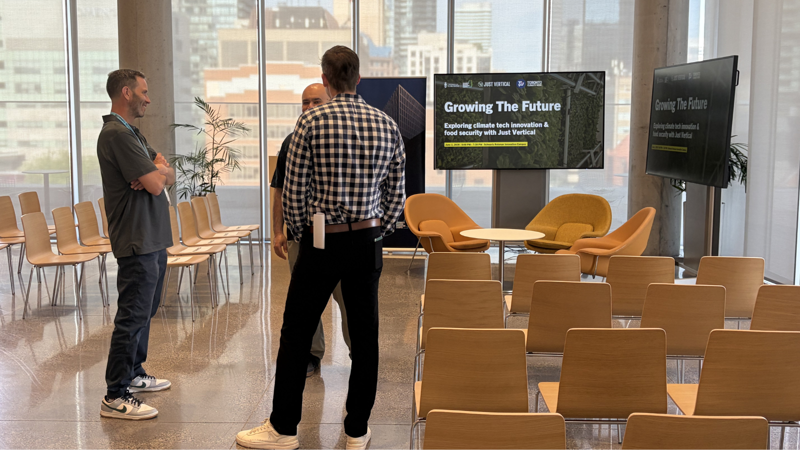 Conner Tidd and speakers conversing in a bright, modern room filled with empty audience chairs. In the background, presentation screens display slides titled "Growing The Future: Exploring climate tech innovation & food security with Just Vertical."