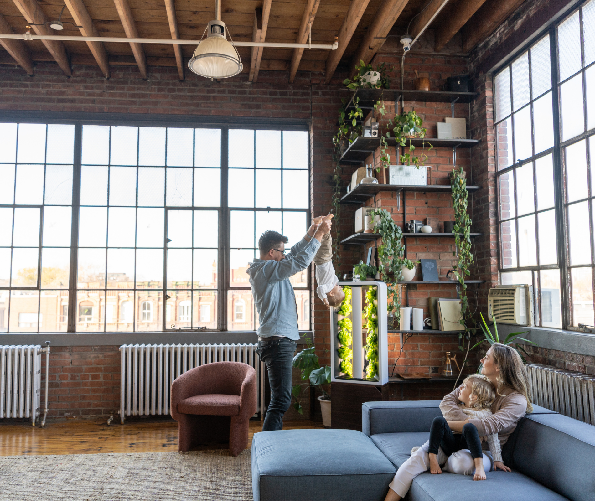 A family standing together around a Just Vertical indoor hydroponic farm tower growing fresh produce in a home living space.